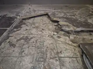 Close-up of lifted wet room tile showing a large unsupported void beneath the tile